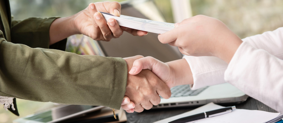 Business people shaking hands, finishing up meeting. businessman giving money to his partner while making contract - bribery and corruption concepts.