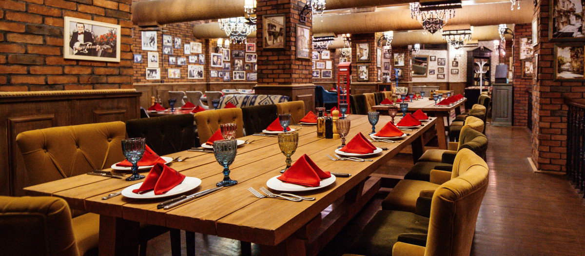 a restaurant hall with red brick walls wooden tables and pipes in the ceiling