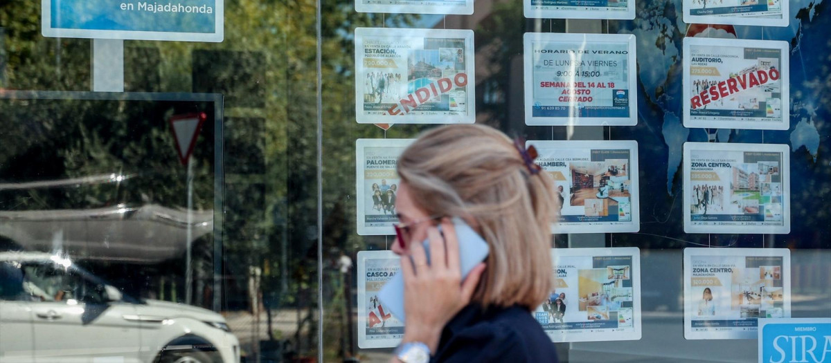 Una mujer camina frente a un escaparate de anuncios de viviendas.