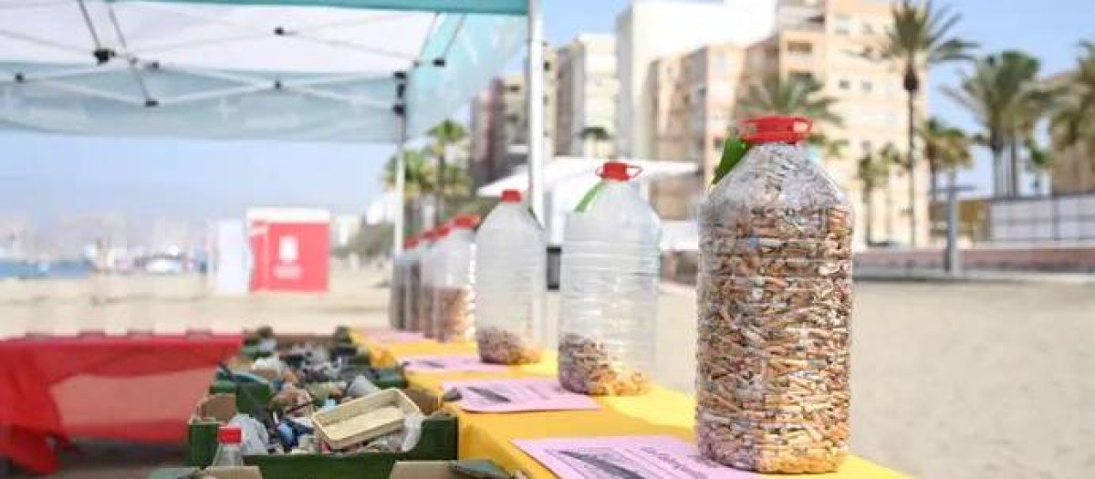 Botellas llenas de colillas y cajas con residuos recogidos del arenal, expuestas en la playa