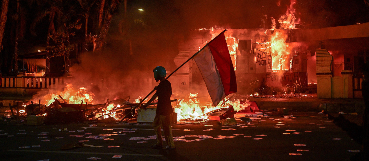 Un manifestante indonesio porta una bandera frente a un edificio en llamas