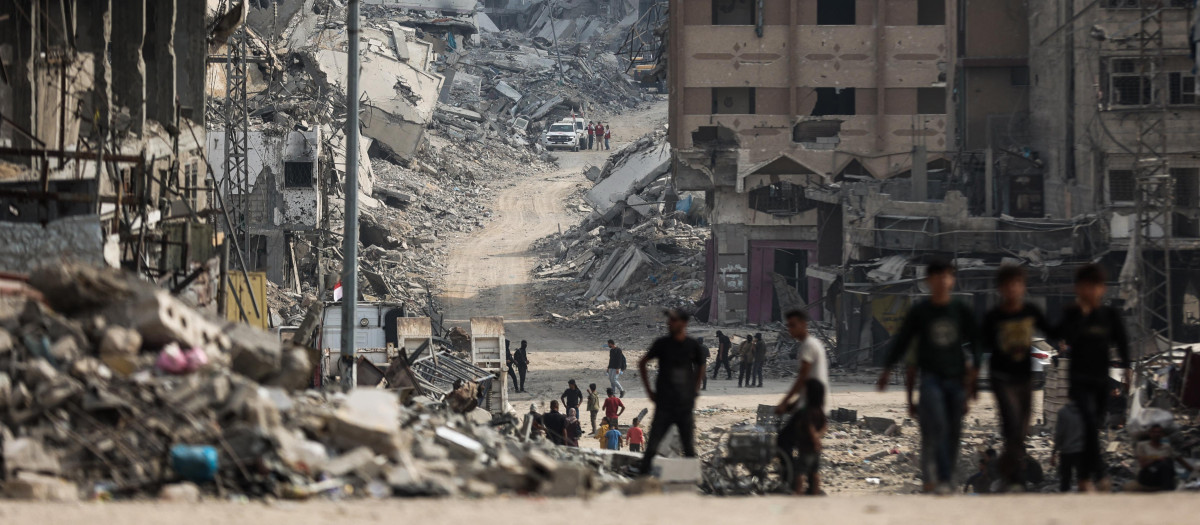 Palestinos caminan cerca de una zona donde militantes de Hamás y miembros del Comité Internacional de la Cruz Roja (CICR) (al fondo) buscan los cuerpos de rehenes israelíes entre los escombros de la ciudad de Gaza el 3 de noviembre de 2025.