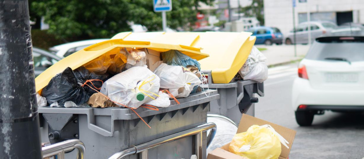 Una mujer camina junto a contenedores llenos de basura.