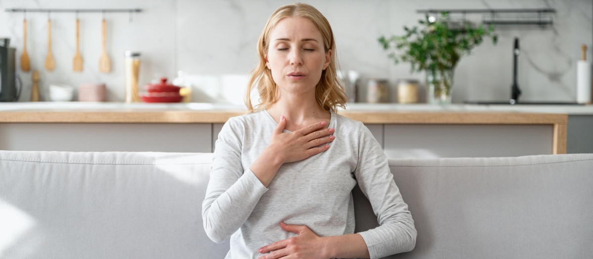Concept of mental health. Woman sitting on couch and doing calming breathing exercises after panic attack. Female inhaling and exhaling to deep breath. Self-control, anxiety relief concept