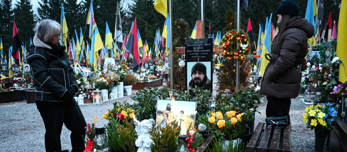 La gente visita la tumba de un soldado ucraniano caído, decorada con árboles de Navidad y adornos de Año Nuevo, en el Cementerio Militar de Lychakiv la víspera de Nochebuena, en Lviv,
