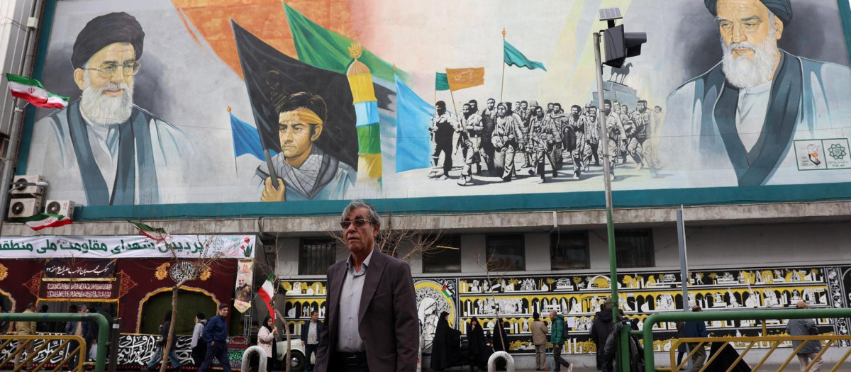 Un hombre pasa junto a un mural que representa al líder supremo iraní, el ayatolá Alí Jamenei (izq., arriba) y al difunto líder supremo, el ayatolá Ruhollah Jomeini