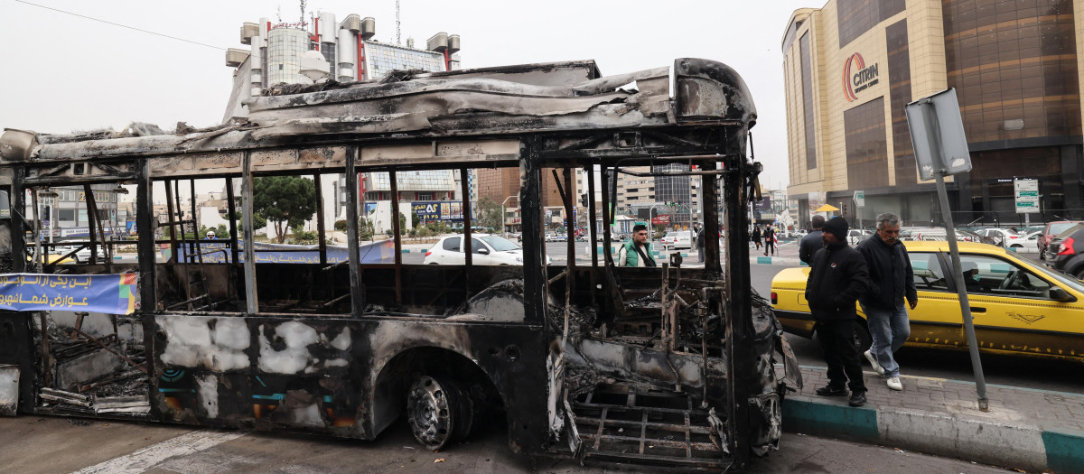 Los restos de un autobús incendiado con una pancarta que dice "Este fue uno de los nuevos autobuses de Teherán, financiado con el dinero de los impuestos del pueblo", en la plaza Sadeghieh de Teherán