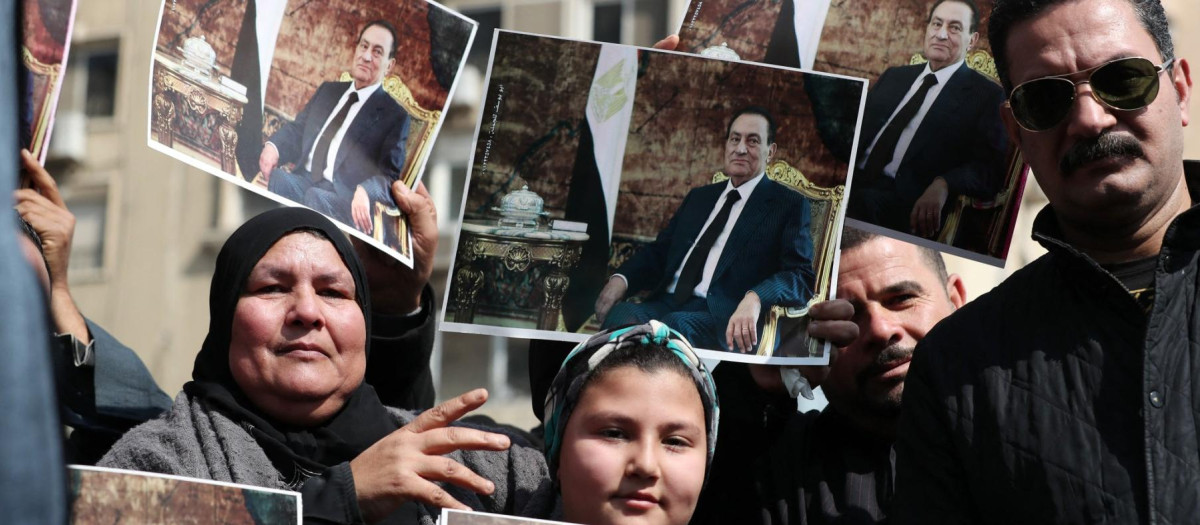Supporters of Egypt's former president Hosni Mubarak hold pictures of the late leader near the family cemetary where he will be buried, in the Heliopolis neighbourhood in the capital Cairo, on February 26, 2020. Mubarak was buried in a trendy Cairo suburb after a military funeral organised by the state to honour his war-time heroics. The former president, who ruled for over 29 years and crafted a lasting image of an autocrat in the region, died on February 25 aged 91 in a Cairo military hospital nine years after he was ousted from power following an 18-day popular uprising. (Photo by Mohamed el-Shahed / AFP)