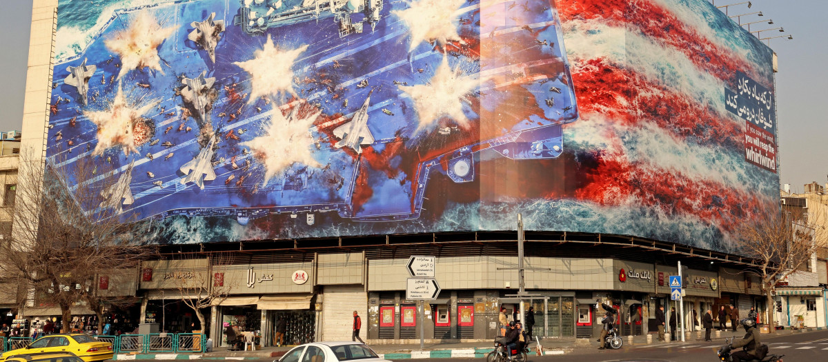 Vehículos pasan junto a una valla publicitaria antiestadounidense instalada en un edificio de la plaza Enqelab, en Teherán