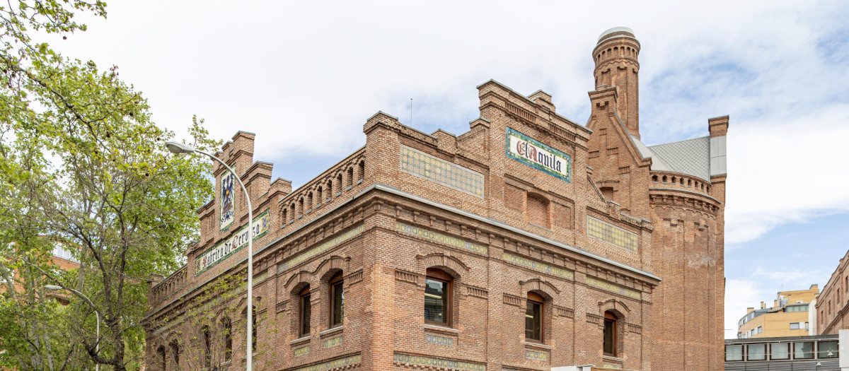 La Comunidad de Madrid ha declarado Bien de Interés Cultural a la antigua fábrica de cerveza ‘El Águila’, actual sede del Archivo y la Biblioteca Regional. Creado en 1912 por el arquitecto Eugenio Jiménez Corera y de estilo neomudéjar, está considerado como uno de los edificios más emblemáticos y mejor conservados de la arquitectura industrial madrileña de principios del siglo XX. 


La Comunidad busca garantizar la conservación de los elementos arquitectónicos originales de los siete pabellones que integran el conjunto, destacando los muros perimetrales de la fachada, las cubiertas de madera del pabellón de los primeros silos y, de forma parcial, las correspondientes a la zona destinada a maltería. 

De similar apariencia a otros inmuebles como los almacenes de Tabacalera o la fábrica de Mahou en la calle Amaniel, esta fábrica llegó a tener, en la segunda década del siglo XX, un 25% de cuota de mercado en su sector. Esto ocurrió antes de que el Gobierno de la República la incautase, siendo recuperada posteriormente a la Guerra Civil. Pasado el tiempo y, a causa de tener que adaptarse a las nuevas necesidades productivas, se produjeron algunas ampliaciones. Lo más destacable fue la construcción de un edificio de talleres en la esquina de las calles Bustamante y Vara del Rey. 

Otros cambios fueron los de los sectores este y oeste, siendo este último actualmente la Biblioteca Regional Joaquín Leguina. Por su parte, el ala esta se destinaba a las bodegas, un edificio de tres alturas dedicado al envasado y almacenamiento del producto. En cuanto al centro de la parcela, se sitúa el Archivo Regional. Finalmente, en los años 80 cesó su actividad y quedó abandonada hasta el año 1993, cuando pasó a integrarse en el patrimonio del Ejecutivo regional. 

La Comunidad de Madrid ha declarado Bien de Interés Cultural a la antigua fábrica de cerveza ‘El Águila’, actual sede del Archivo y la Biblioteca Regional. Creado en 1912 por el arquitecto Eugenio Jiménez Corera y de estilo neomudéjar, está considerado como uno de los edificios más emblemáticos y mejor conservados de la arquitectura industrial madrileña de principios del siglo XX. 


La Comunidad busca garantizar la conservación de los elementos arquitectónicos originales de los siete pabellones que integran el conjunto, destacando los muros perimetrales de la fachada, las cubiertas de madera del pabellón de los primeros silos y, de forma parcial, las correspondientes a la zona destinada a maltería. 

De similar apariencia a otros inmuebles como los almacenes de Tabacalera o la fábrica de Mahou en la calle Amaniel, esta fábrica llegó a tener, en la segunda década del siglo XX, un 25% de cuota de mercado en su sector. Esto ocurrió antes de que el Gobierno de la República la incautase, siendo recuperada posteriormente a la Guerra Civil. Pasado el tiempo y, a causa de tener que adaptarse a las nuevas necesidades productivas, se produjeron algunas ampliaciones. Lo más destacable fue la construcción de un edificio de talleres en la esquina de las calles Bustamante y Vara del Rey. 

Otros cambios fueron los de los sectores este y oeste, siendo este último actualmente la Biblioteca Regional Joaquín Leguina. Por su parte, el ala esta se destinaba a las bodegas, un edificio de tres alturas dedicado al envasado y almacenamiento del producto. En cuanto al centro de la parcela, se sitúa el Archivo Regional. Finalmente, en los años 80 cesó su actividad y quedó abandonada hasta el año 1993, cuando pasó a integrarse en el patrimonio del Ejecutivo regional.
