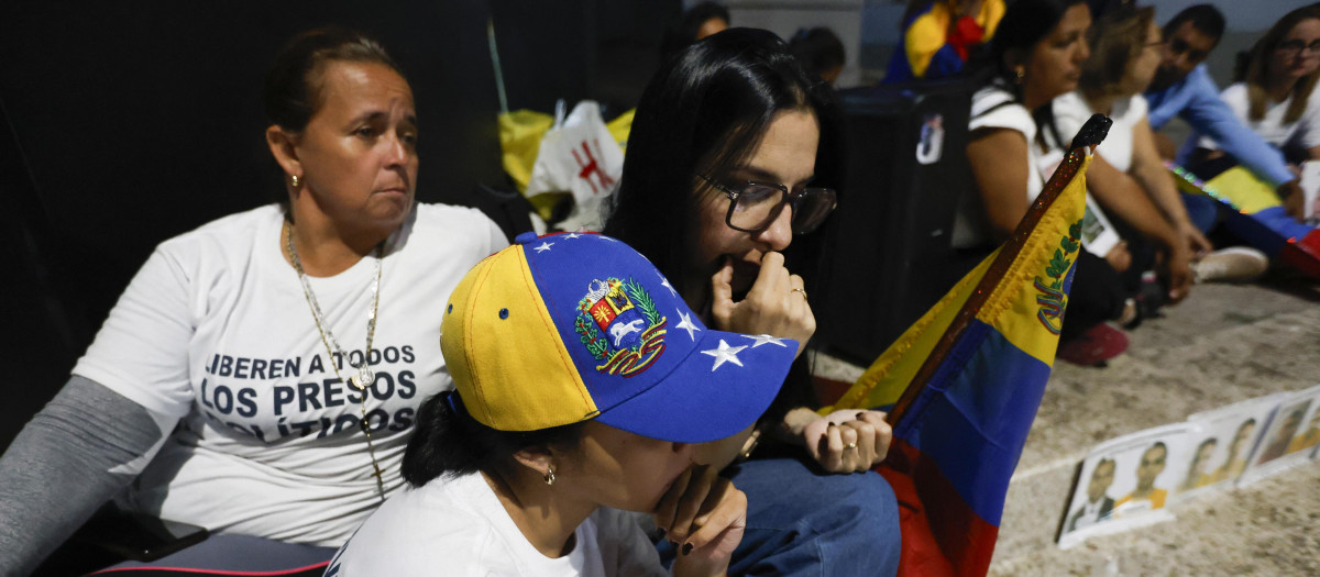 Familiares de presos políticos miran en un teléfono celular la transmisión en vivo del presidente de la Asamblea Nacional de Venezuela, Jorge Rodríguez,