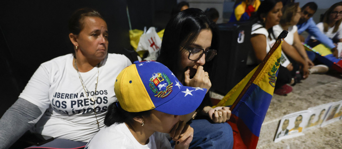 Familiares de presos políticos miran en un teléfono celular la transmisión en vivo del presidente de la Asamblea Nacional de Venezuela, Jorge Rodríguez,