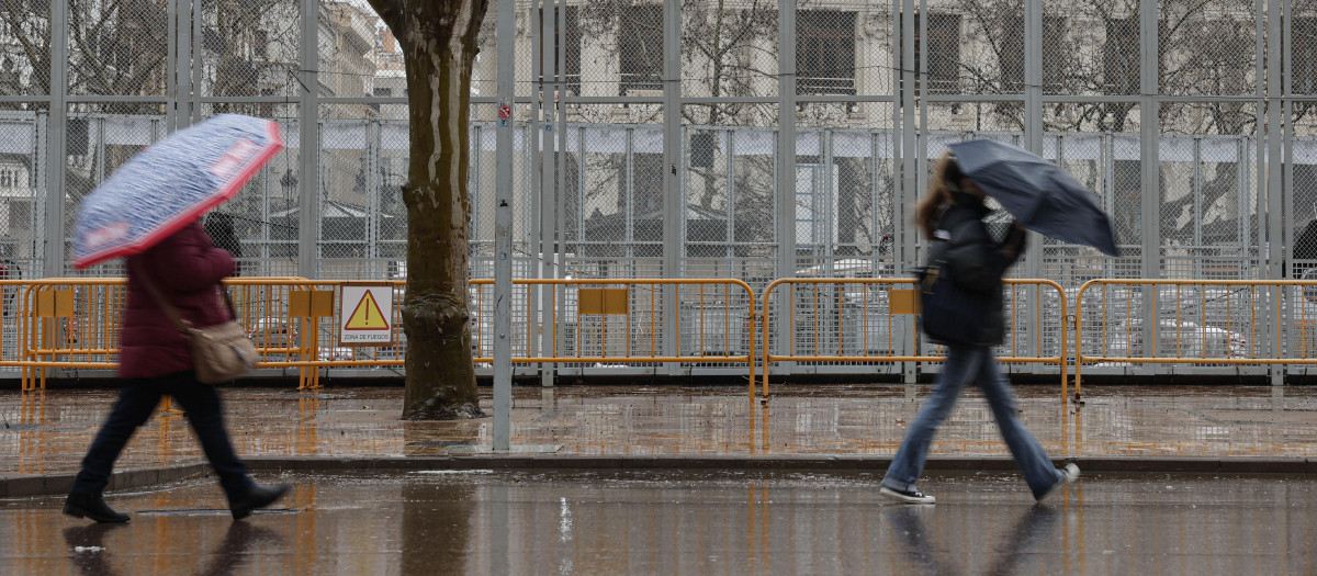 Imagen de varias personas pasando con paraguas por delante de la zona de la mascletà de las Fallas de Valencia.