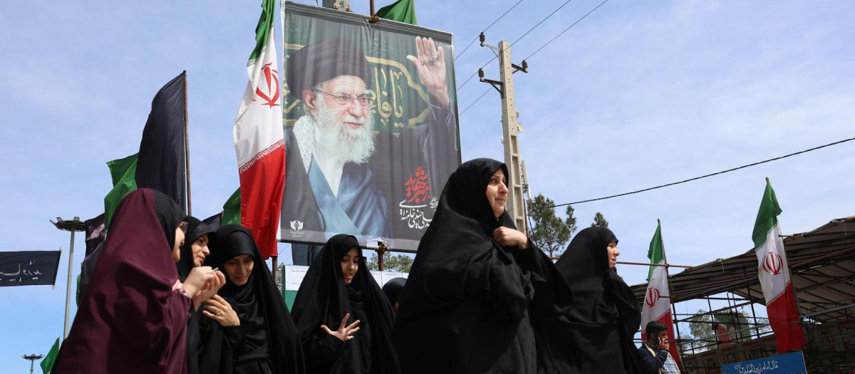 Mujeres iraníes caminan cerca de un cartel del difunto líder supremo iraní, el ayatolá Ali Khamnei, durante el funeral de las víctimas del conflicto entre Irán, Israel y Estados Unidos, en el cementerio Behesht Zahra, al sur de Teherán, Irán,