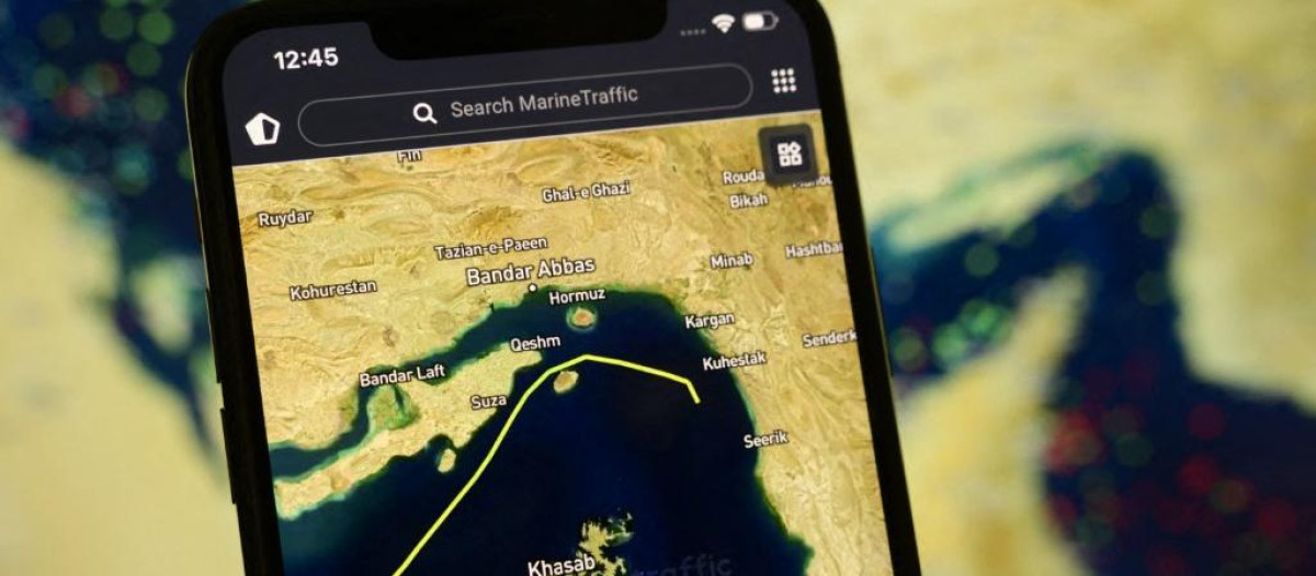 Un teléfono inteligente muestra la aplicación MarineTraffic, que muestra un buque cruzando el estrecho de Ormuz, con una vista satelital del estrecho y numerosas balizas de barcos al fondo