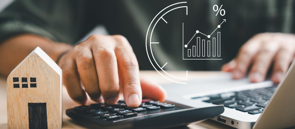 Hand using calculators, planning home refinance. Wooden house model, buy or rent note, calculators on desk. Saving for property purchase, mortgage payment. Tax, credit analysis for financial benefit.