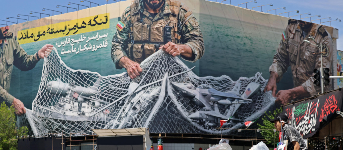 Un vendedor empuja su carrito junto a una valla publicitaria gigante que dice "El estrecho de Ormuz permanece cerrado" en la Plaza de la Revolución en Teherán e