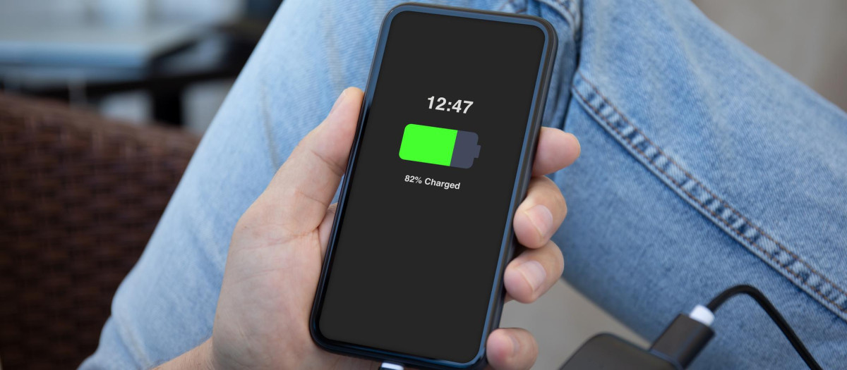 Man hands holding phone with charged battery on the screen connected to powerbank charge