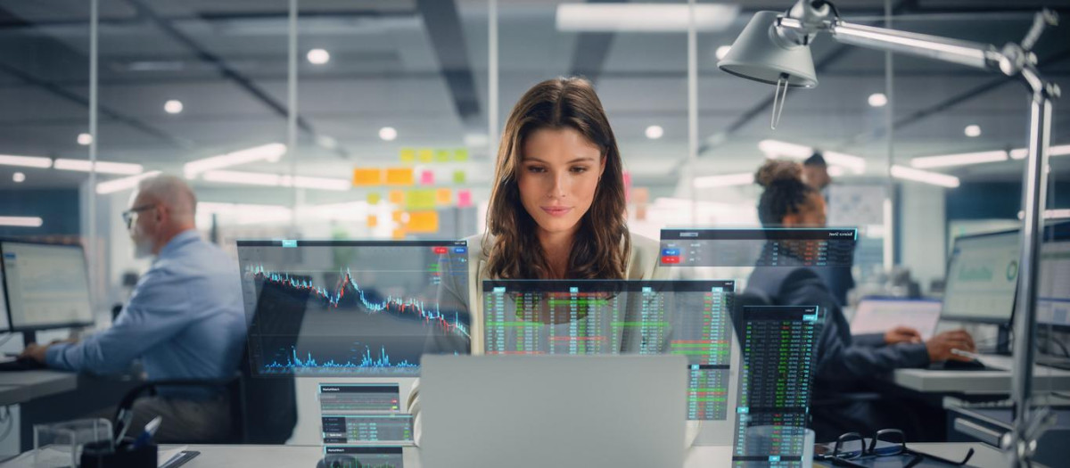 Young Happy Businesswoman Using Laptop Computer in Modern Office with Colleagues. Stylish Beautiful Financial Advisor Working. VFX Hologram Edit Visualizing Stock Exchange Interface, Opened Charts.