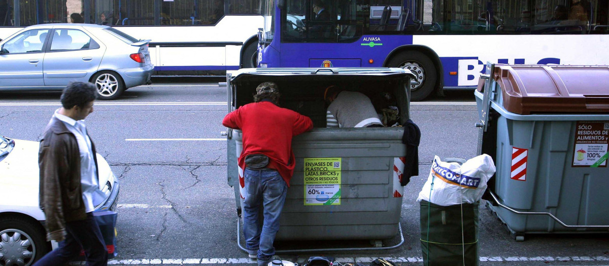 Dos personas recopilan enseres de un contenedor de basura en Valladolid
