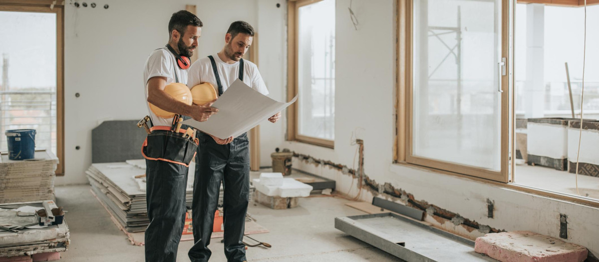 Young manual workers standing at construction site and examining blueprints.