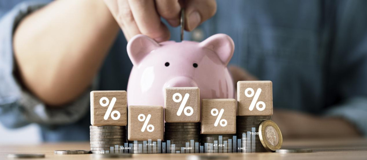 Close-up of a person putting a coin into a pink piggy bank with stacked coins and percentage blocks representing saving money financial growth investment and interest rate concept.