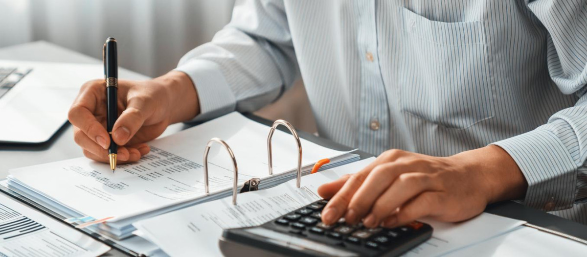 Corporate auditor calculating budget with calculator on his office desk. Dedicated accountant professional of accounting business company analyzing financial document to forecast income. Insight