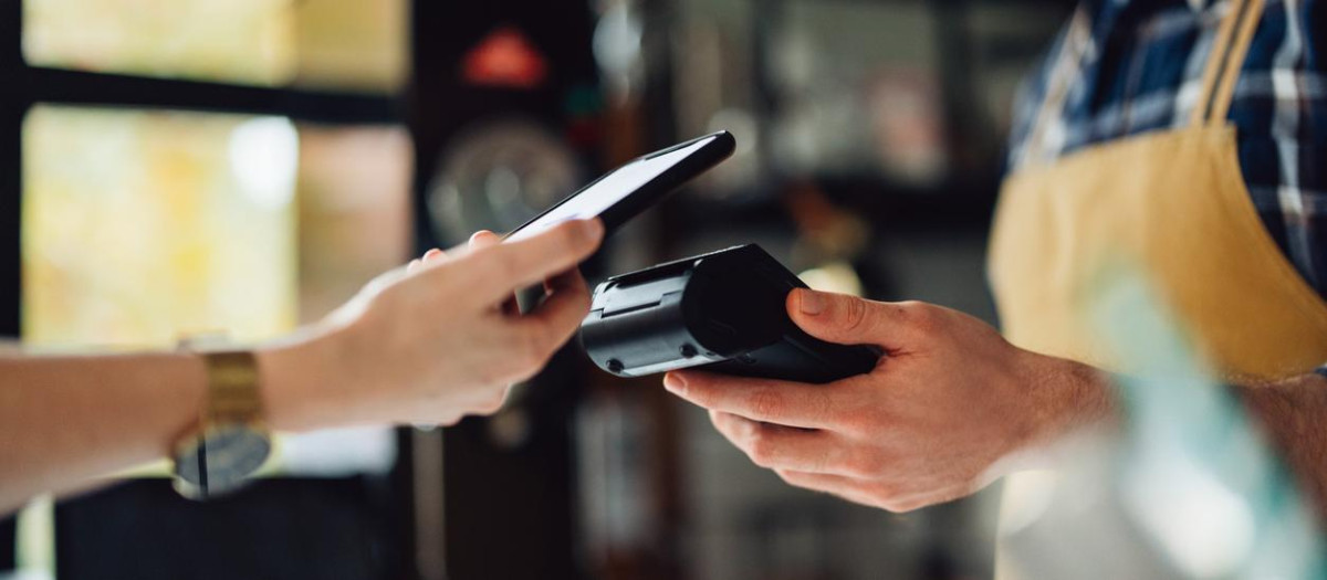Unrecognizable people making an online payment. Anonymous man is holding a card machine while the other person is placing their phone to pay.