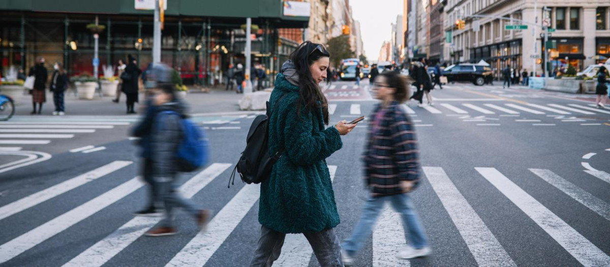Woman in her 30s commuting through the streets of Manhattan, New York City. She is wearing a fake fur coat, on a sunny but cold winter day, checking messages on her smartphone.