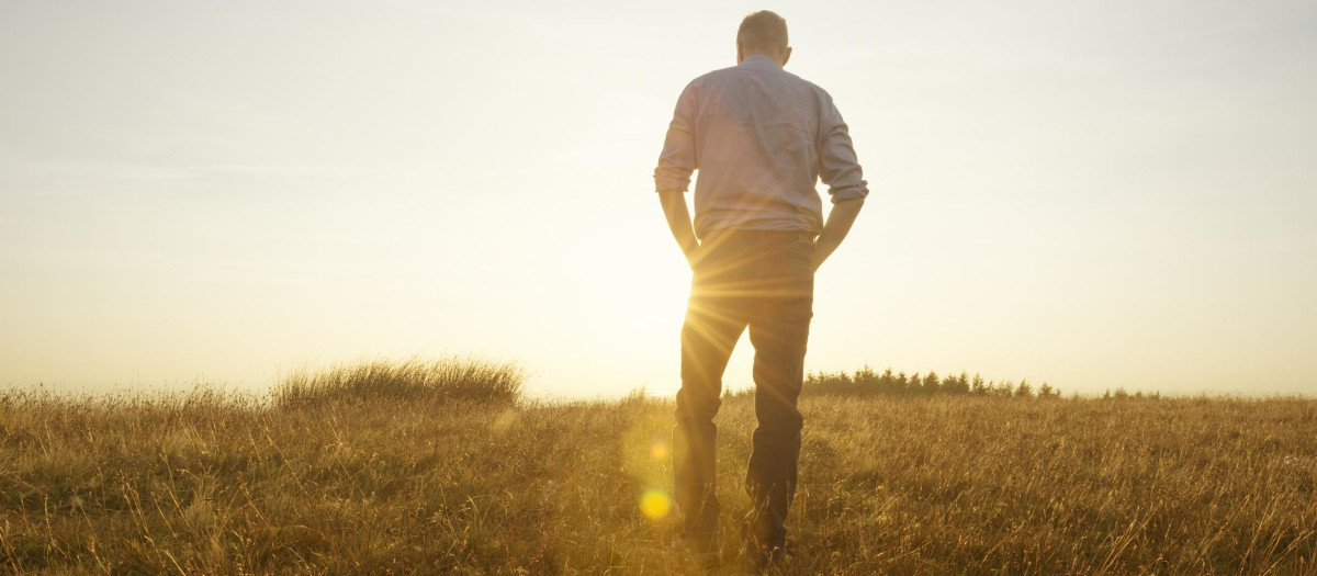 Man walking in the countryside looking at the sunset, strong lens flare from the late afternoon autumn sun.