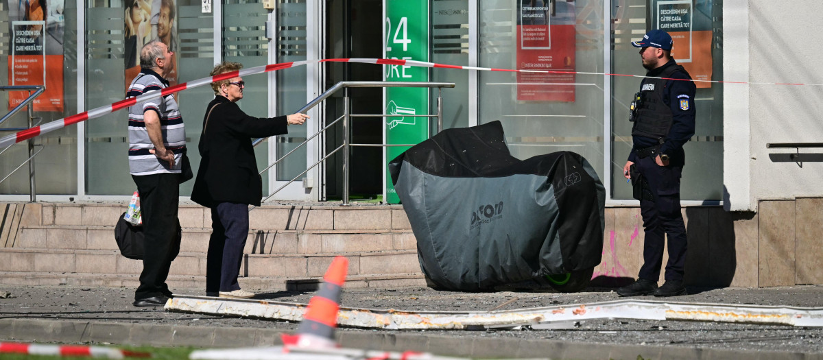 Residentes locales conversan con un gendarme mientras permanecen junto a los escombros y la zona acordonada en la calle tras el impacto de un dron ruso contra un edificio de apartamentos en Galati, al este de Rumania.