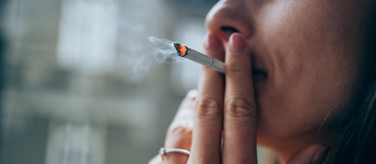 Unrecognizable young woman enjoying a cigarette outdoors. Focus is on the cigarette.
