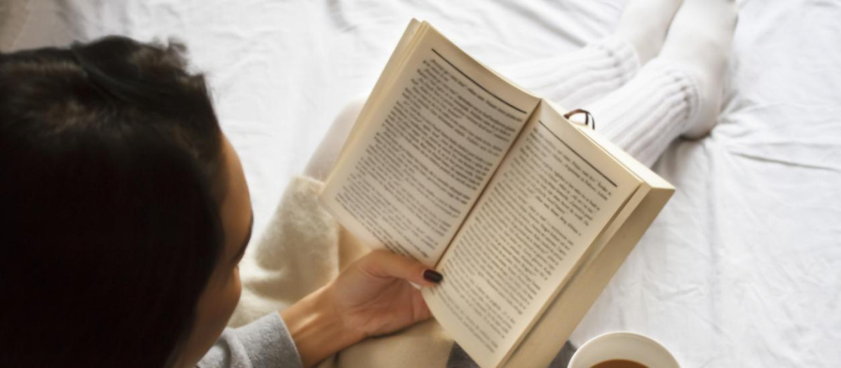 beautiful brunette girl reading book and drinking coffee in bed in the morning