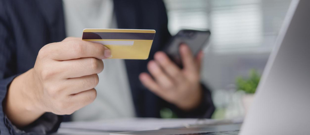 Customer verifies online purchase with credit card and smartphone at office desk near laptop, mobile payment ecommerce banking secure transaction convenience concept