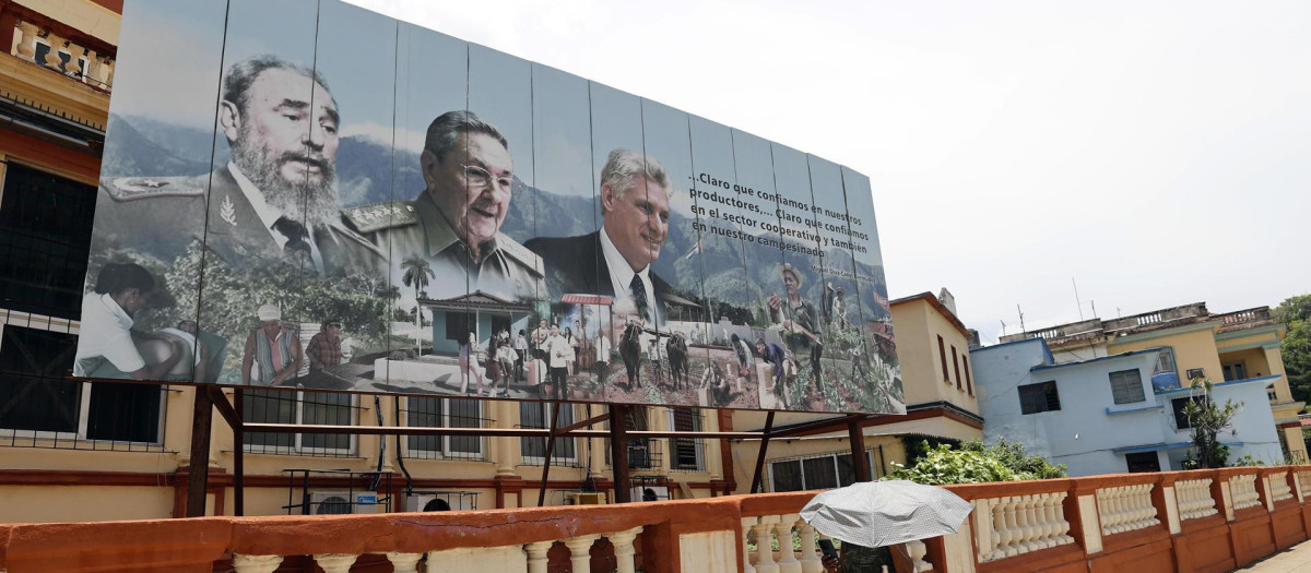Una mujer camina frente a una valla que muestra las imágenes del presidente de Cuba, Miguel Diaz-Canel (d), el general y expresidente Raúl Castro (c), y el fallecido expresidente de Cuba Fidel Castro (i), este lunes en La Habana (Cuba).