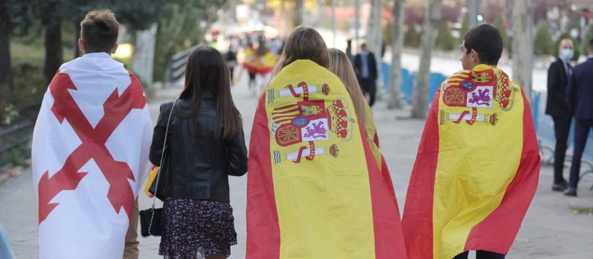 Varios jóvenes se dirigen al desfile del 12 de octubre. En la imagen se pueden distinguir dos banderas: la bandera de España, y la Cruz de Borgoña