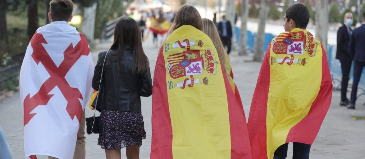 Varios jóvenes se dirigen al desfile del 12 de octubre. En la imagen se pueden distinguir dos banderas: la bandera de España, y la Cruz de Borgoña