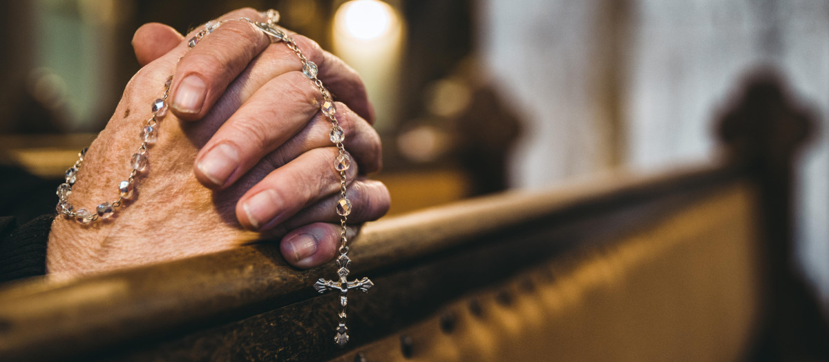 Praying senior hands with rosary in church bench