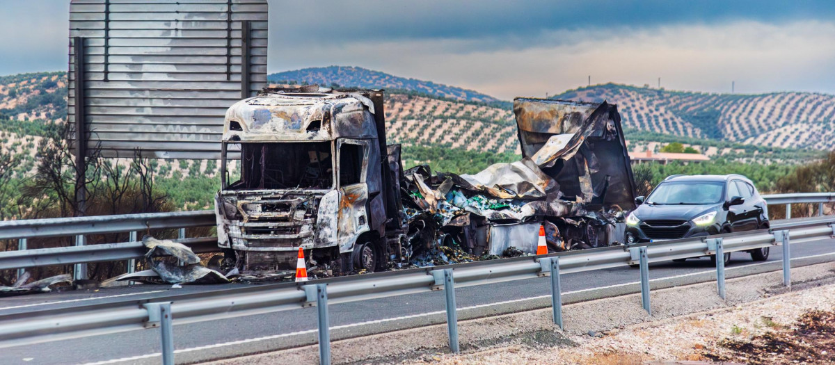 Completely burned-out truck after catching fire on the road, highway with olive fields in the background.