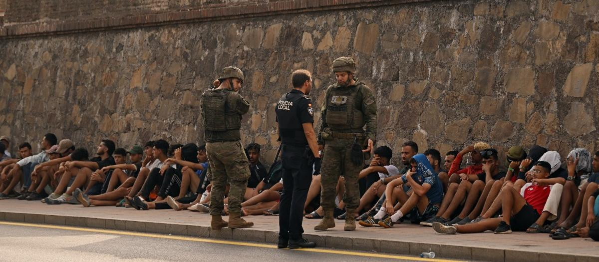 Soldados españoles conversan mientras observan a inmigrantes sentados en el suelo, antes de escoltarlos de regreso a Marruecos