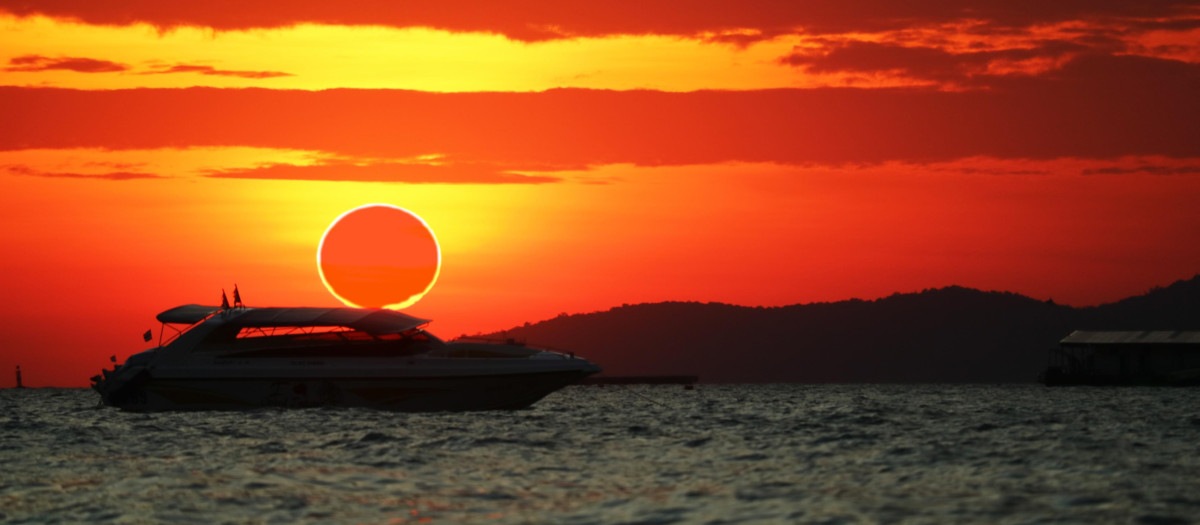 Fenómeno increíble de eclipse de sol parcial sobre barco de silueta en el mar y el cielo de la puesta de so
