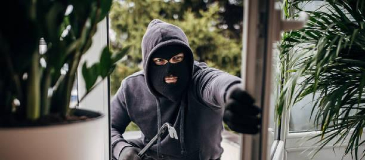 One man, criminal dressed all in black with crowbar, breaking in through window in house