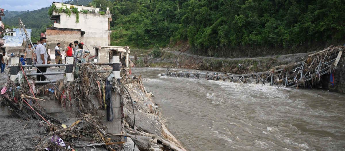Unas personas permanecen cerca de un puente colapsado tras unas inundaciones repentinas en Devighat, en el distrito nepalí de Nuwakot