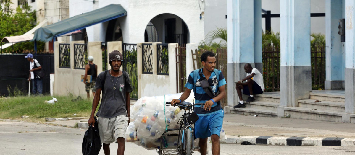 Dos personas caminan por una calle recogiendo envases vacíos para reciclarlos, este martes en la Habana (Cuba)