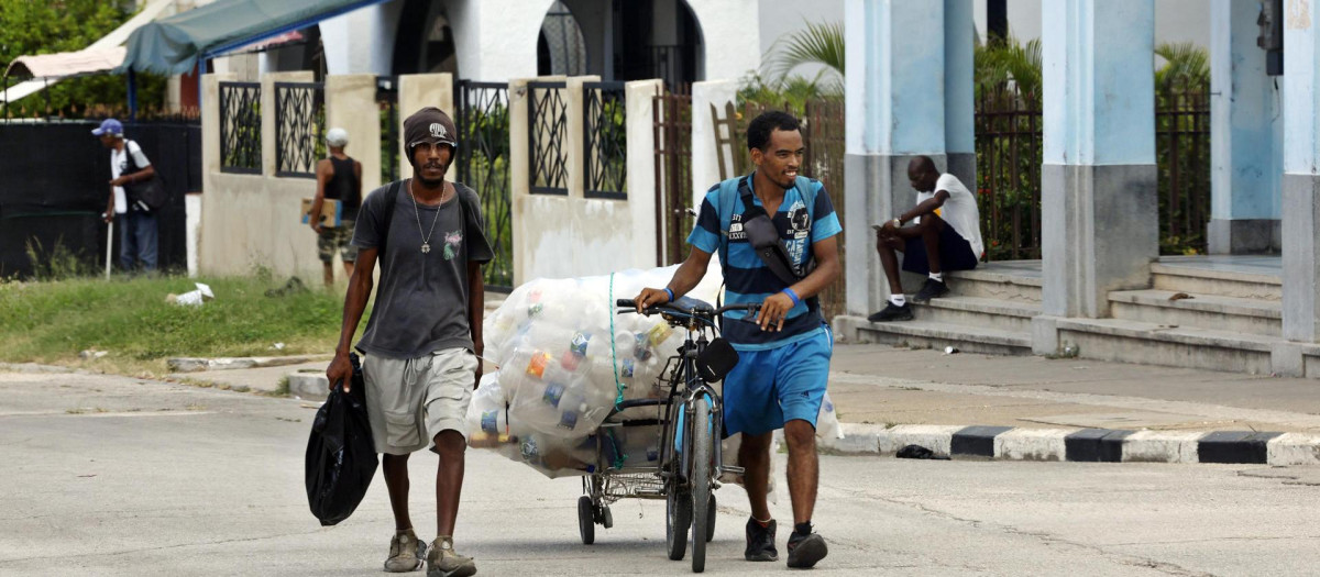 Dos personas caminan por una calle recogiendo envases vacíos para reciclarlos, este martes en la Habana (Cuba)