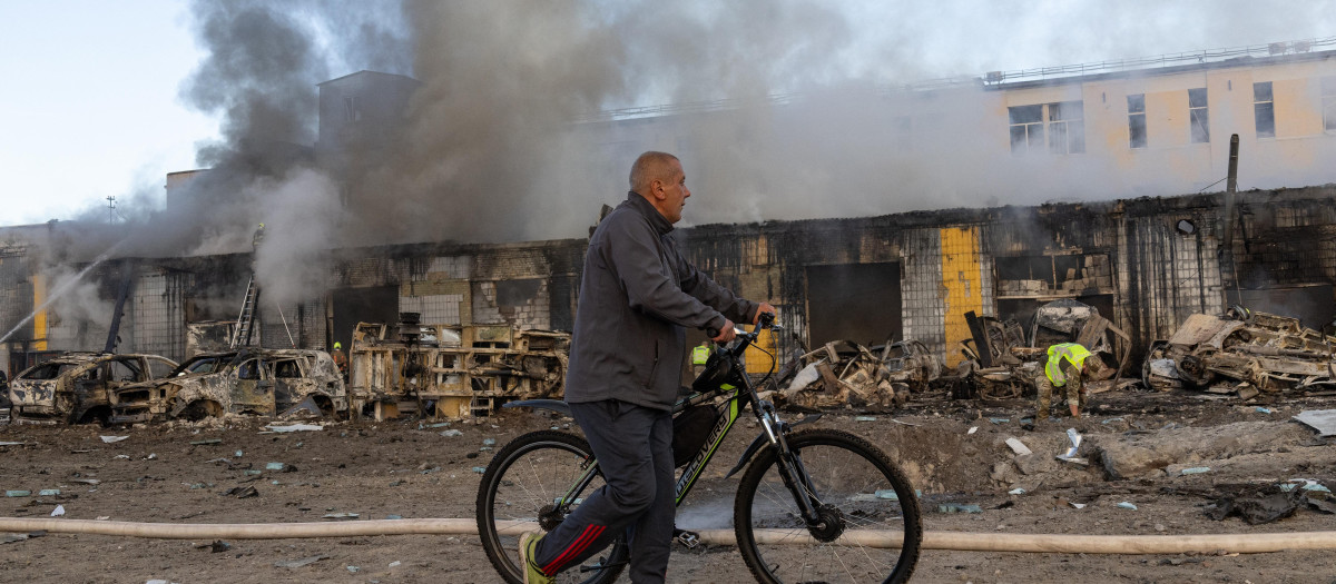 Un hombre carga su bicicleta mientras pasa junto a bomberos que extinguen un incendio tras los ataques con misiles rusos en Kiev