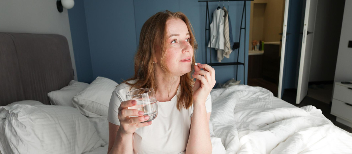 Una mujer tomando una pastilla en la cama