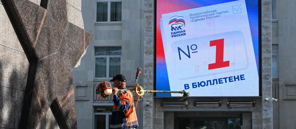 Un hombre con una cortadora de césped pasa junto a una pantalla digital en el edificio de la sede del partido Rusia Unida, que llama a la gente a votar por los candidatos del partido en las próximas elecciones para la cámara baja del parlamento ruso, la Duma Estatal, en Moscú,