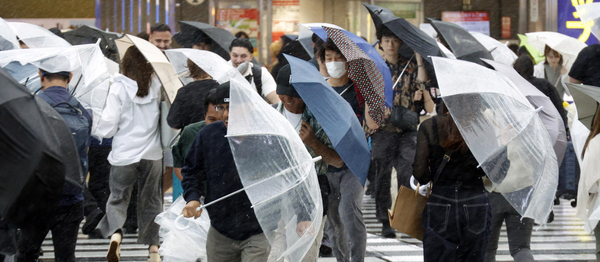 Unos peatones con paraguas cruzan una calle cerca de la estación de Shinjuku bajo fuertes lluvias provocadas por el tifón Dujuan en Tokio