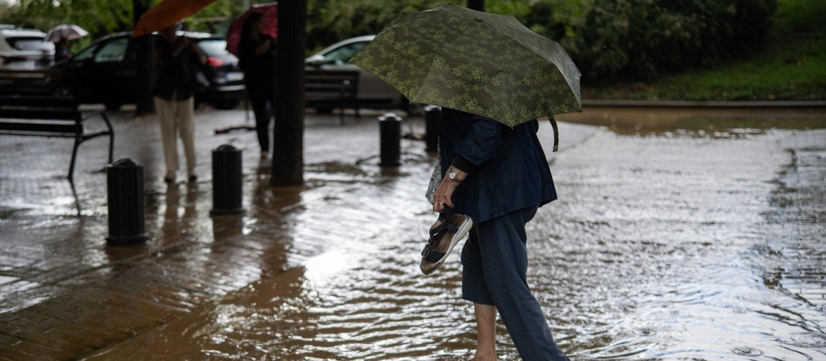 Una mujer cruza a través de la lluvia acumulada en la calle en el barrio de Canyelles-Nou Barris